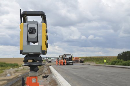 Totální stanice „zaměřuje“ komunikační hranol Trimble MT900 na hladicí liště finišeru a změřené souřadnice posílá do řídicí jednotky nivelačního systému, která tyto informace porovná s digitálním modelem terénu a v případě potřeby provede úpravu výšky nebo příčného sklonu hladicí lišty finišeru.