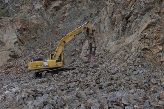 Pásové rypadlo Komatsu s hydraulickým kladivem při druhotném rozpojování horniny v kamenolomu.